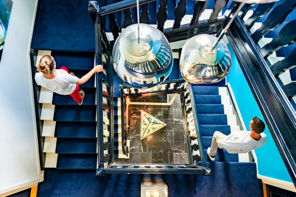 Twee mensen navigeren een complexe, blauwe trap. Dit symboliseert hoe Legian helpt bij Business IT alignment om overzicht te creëren in complexe IT-landschappen.